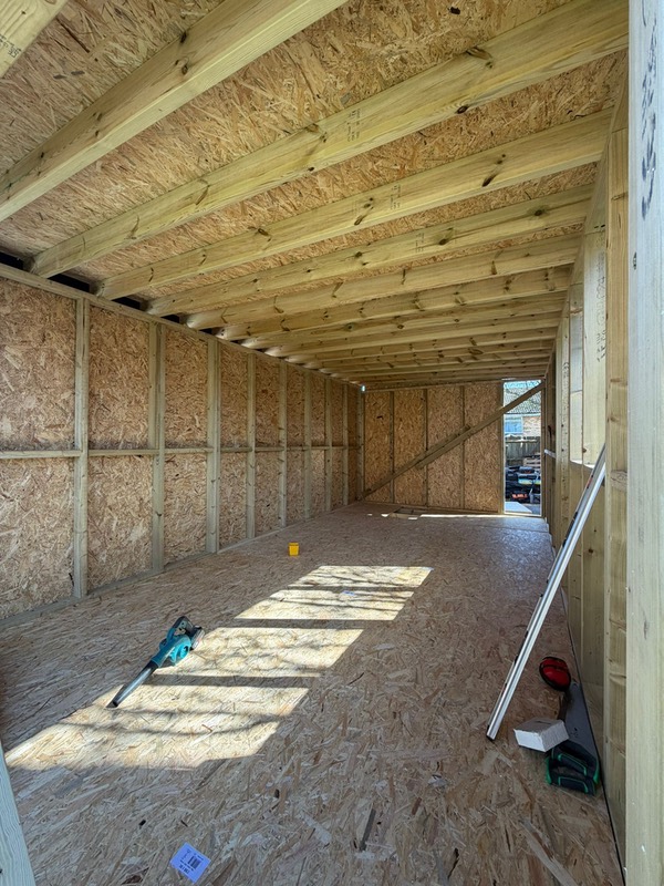  Internal view of a garden room under construction, showcasing the exposed timber stud walls, OSB flooring, and heavy-duty ceiling joists 
