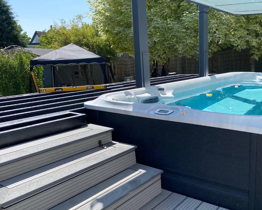 Hot tub installed on dark grey composite decking with matching steps