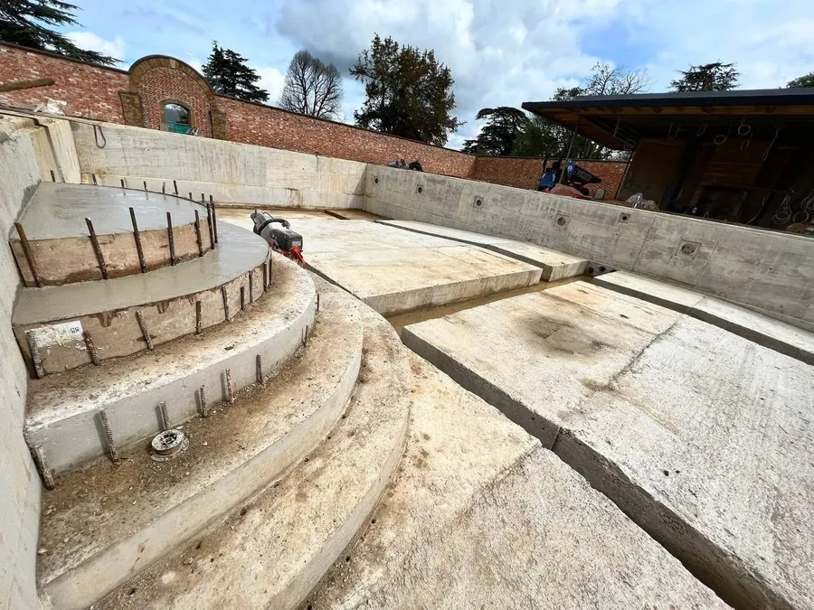 Curved concrete pool shell with formwork and steel reinforcement in a walled garden